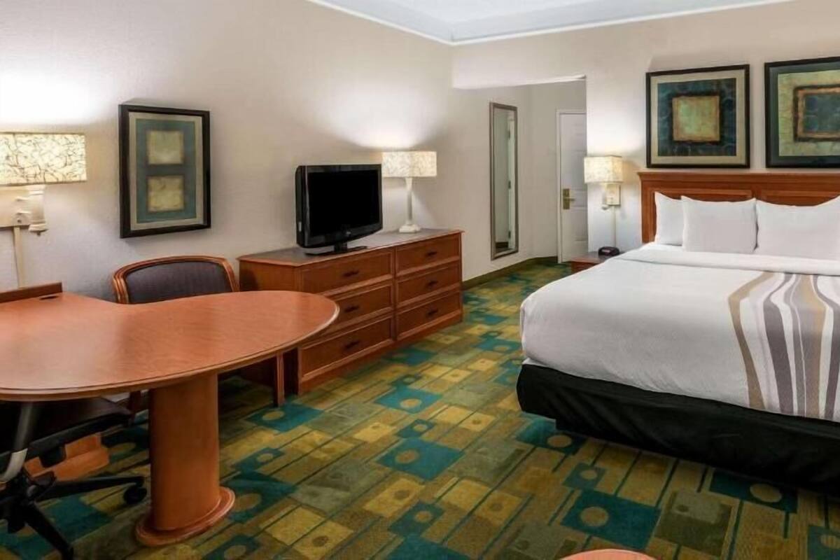 A hotel room with a bed, a desk, a television, and two framed pictures on the wall.