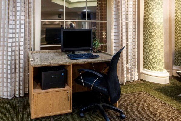 Un espacio de oficina en casa con una computadora de escritorio, una silla de oficina negra, una impresora y una estantería.