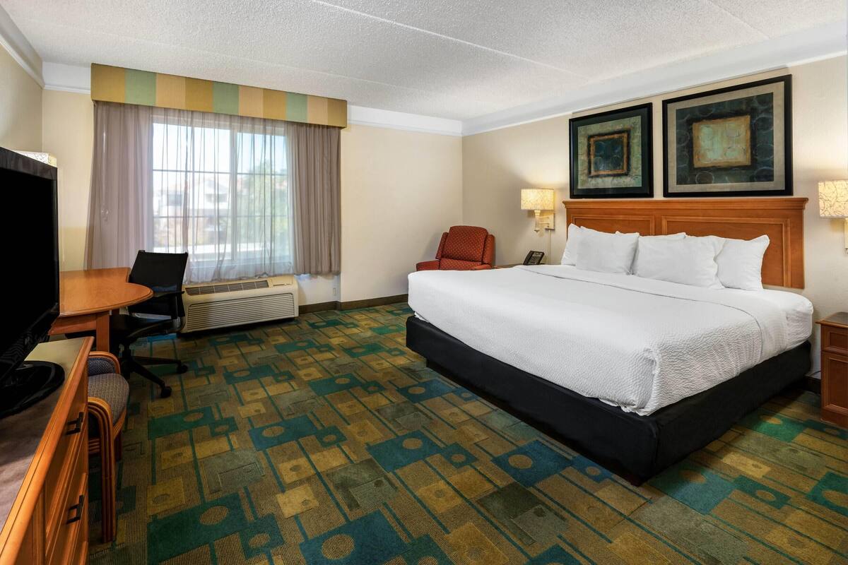 Une chambre d’hôtel équipée d’un lit, d’un bureau, d’une chaise, d’une télévision et d’une fenêtre avec des rideaux.