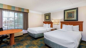 Ein Hotelzimmer mit zwei Betten, einem Schreibtisch und einem Stuhl. An den Wänden hängen zwei Bilder.