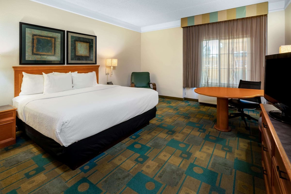 A hotel room with a large bed, a desk, a chair, a television, and two framed pictures on the wall.