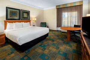 A hotel room with a large bed, a desk, a chair, a television, and two framed pictures on the wall.