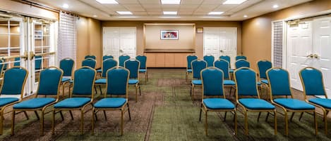 Une salle de conférence avec des rangées de chaises bleues, un sol recouvert de moquette, des portes blanches et un tableau encadré accroché au mur.