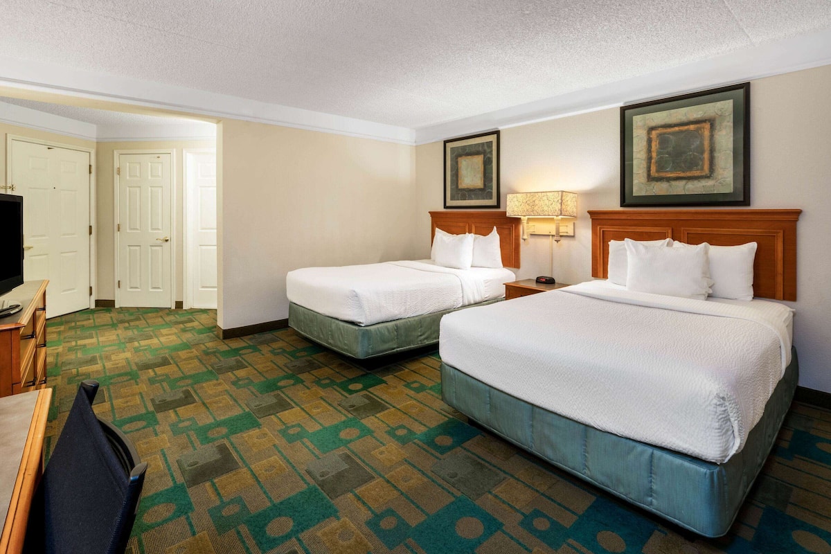 A hotel room with two beds, a desk, a television, and a patterned carpet.