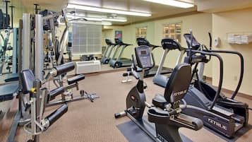Un gimnasio con diverso equipo de ejercicio, incluyendo cintas de correr, una máquina de pesas y una bicicleta estática.