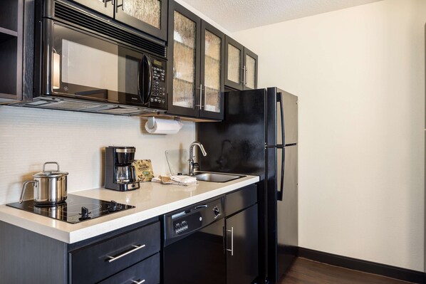 Una cocina moderna con armarios negros, un refrigerador de acero inoxidable, un microondas integrado y una cafetera.