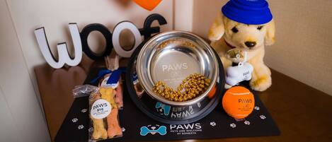 A table with a dog bowl, a toy, a treat bag, and a paw print placemat.