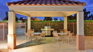 A covered patio area with a grill, seating, and a view of the surrounding greenery.