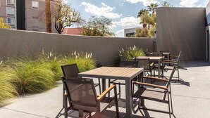 Une terrasse extérieure avec des tables et des chaises, entourée de plantes et d’un petit muret.