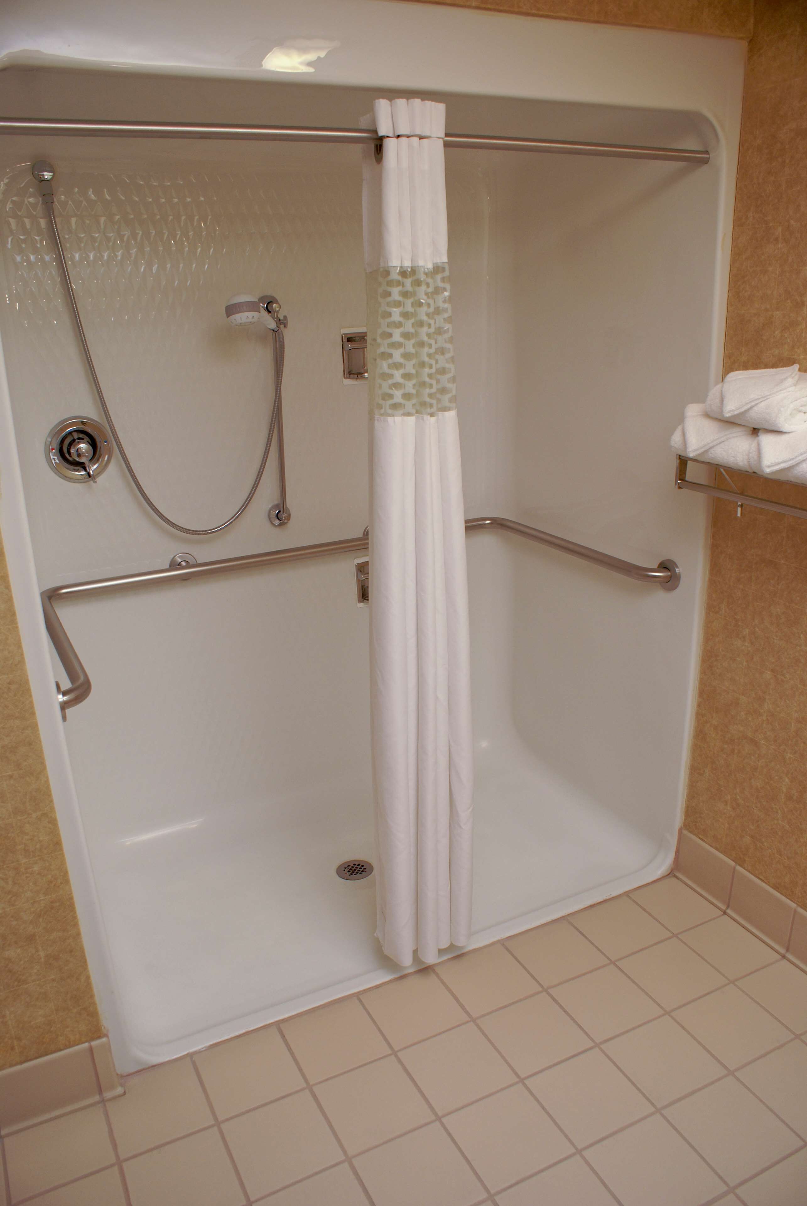 A walk-in shower with a grab bar, a handheld showerhead, and a towel rack.
