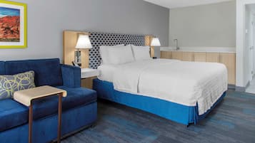 A hotel room with a bed, a blue sofa, a small table, and a nightstand with lamps.