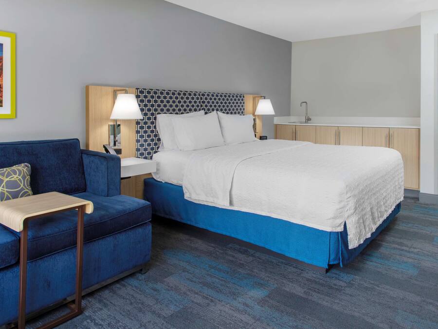 A hotel room with a bed, a blue sofa, a small table, and a nightstand with lamps.