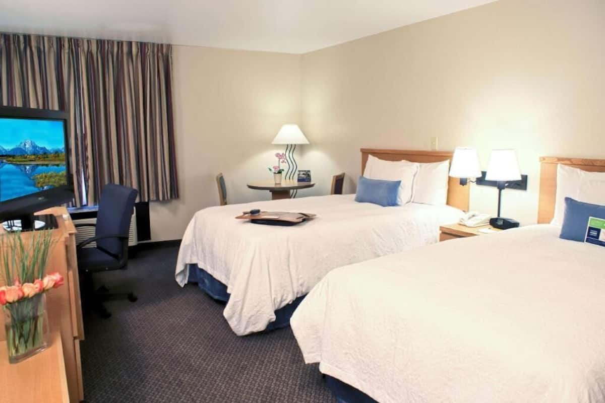 A hotel room with two beds, a desk with a computer, a TV, and a small table with a lamp.