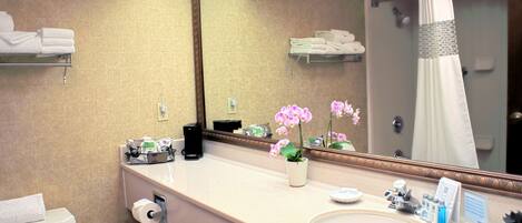 A hotel bathroom with a toilet, sink, mirror, and shower curtain.