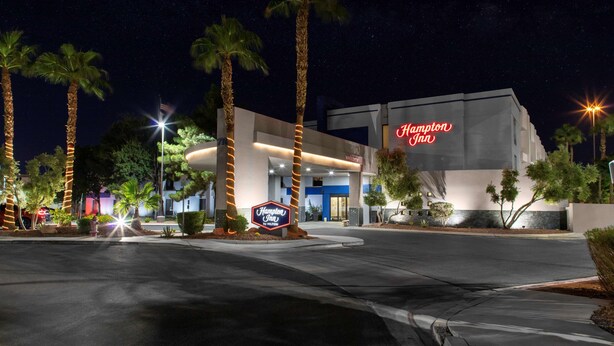 Un hôtel Hampton Inn la nuit, avec des palmiers, une grande enseigne lumineuse et une entrée accueillante.