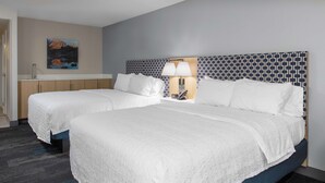 Une chambre d’hôtel avec deux lits, une table de chevet, une lampe et un tableau au mur.