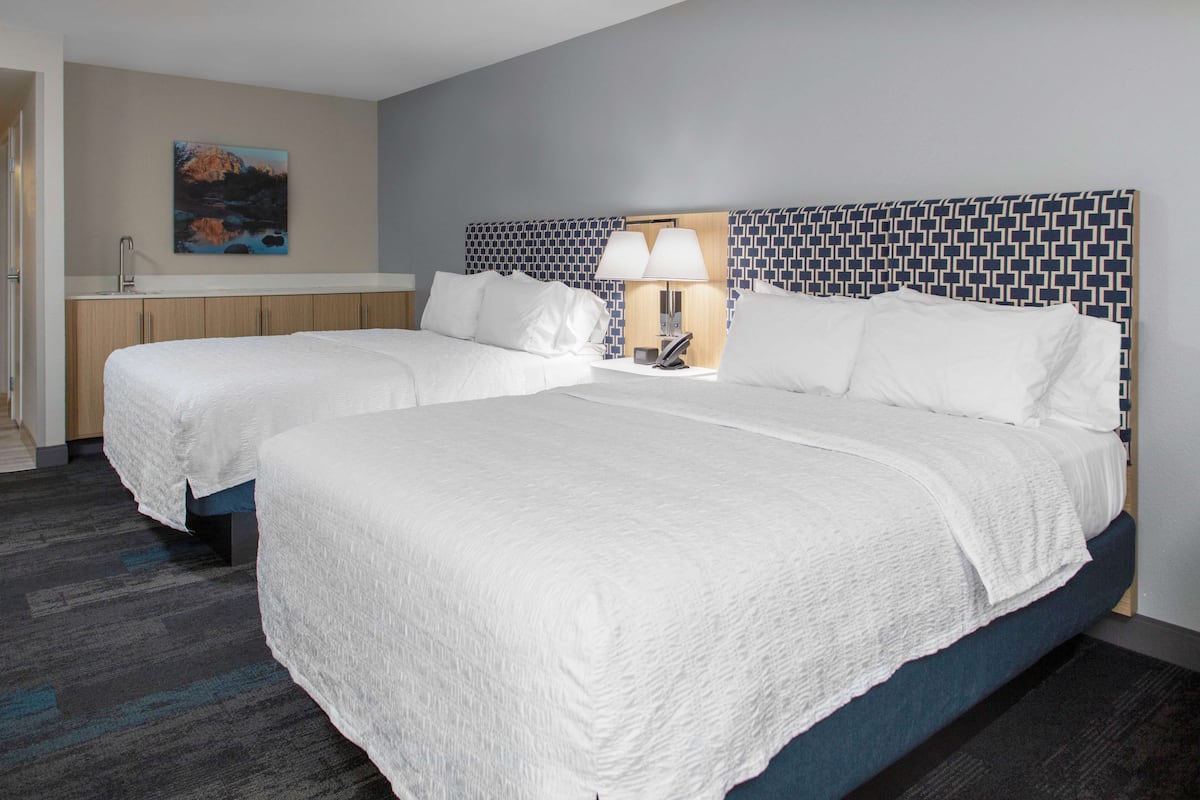 A hotel room with two beds, a nightstand, a lamp, and a painting on the wall.