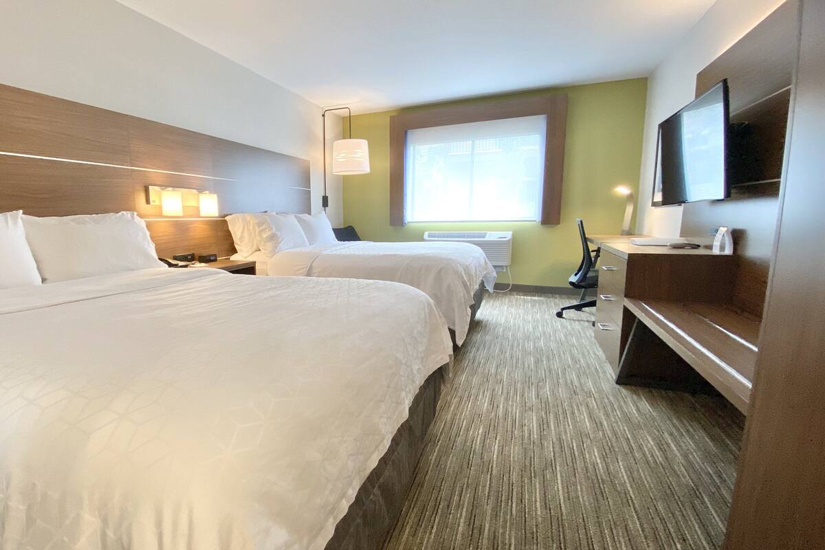 Habitación de hotel con dos camas, un escritorio, una silla, un televisor y una ventana con persianas.