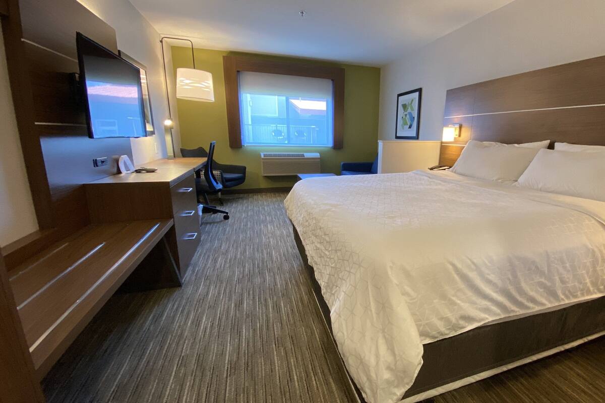 Habitación de hotel con una cama grande, un escritorio con silla, un televisor, una ventana y un cuadro en la pared.
