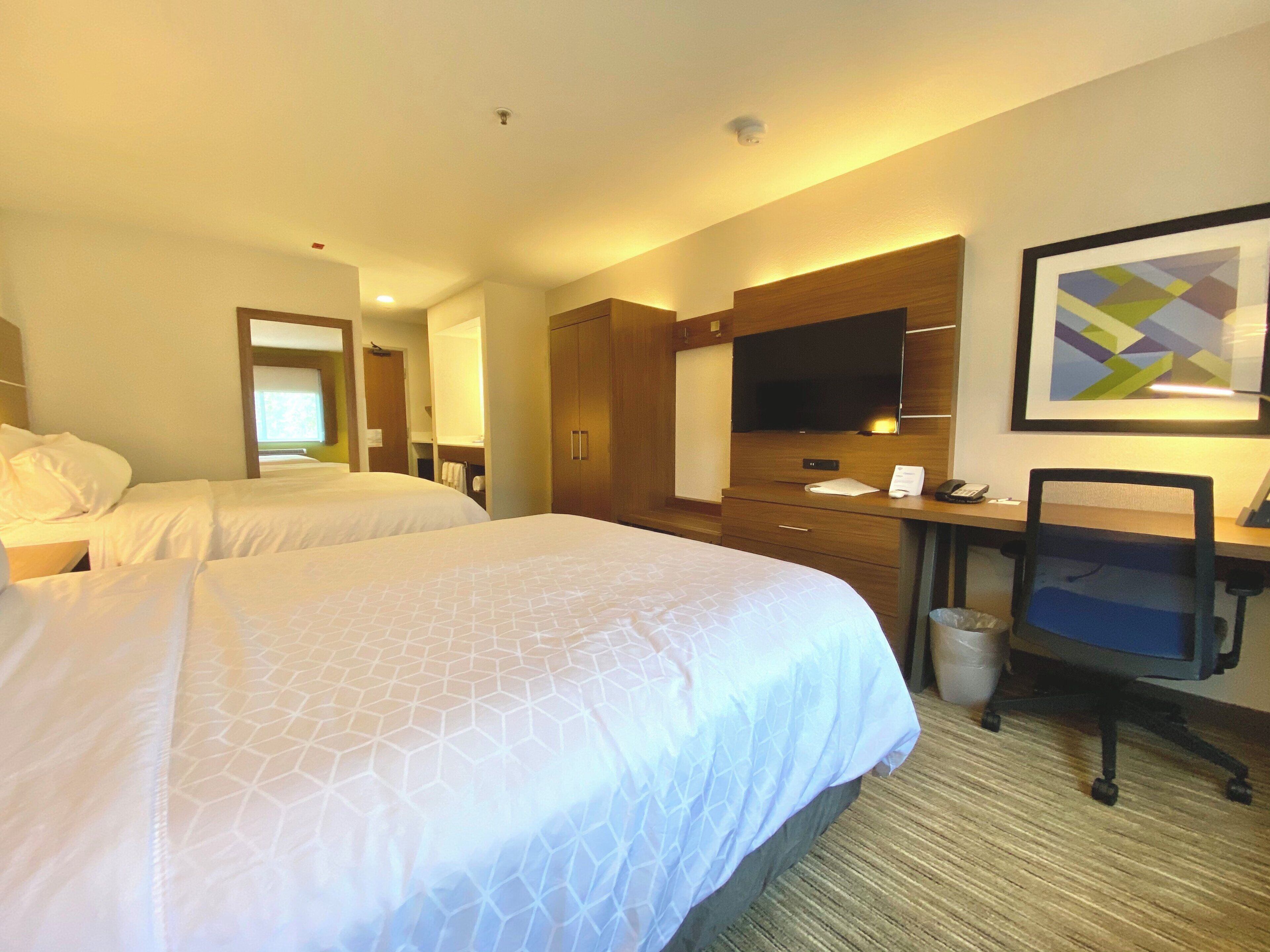 A hotel room with two beds, a desk, a chair, a TV, and a bathroom.