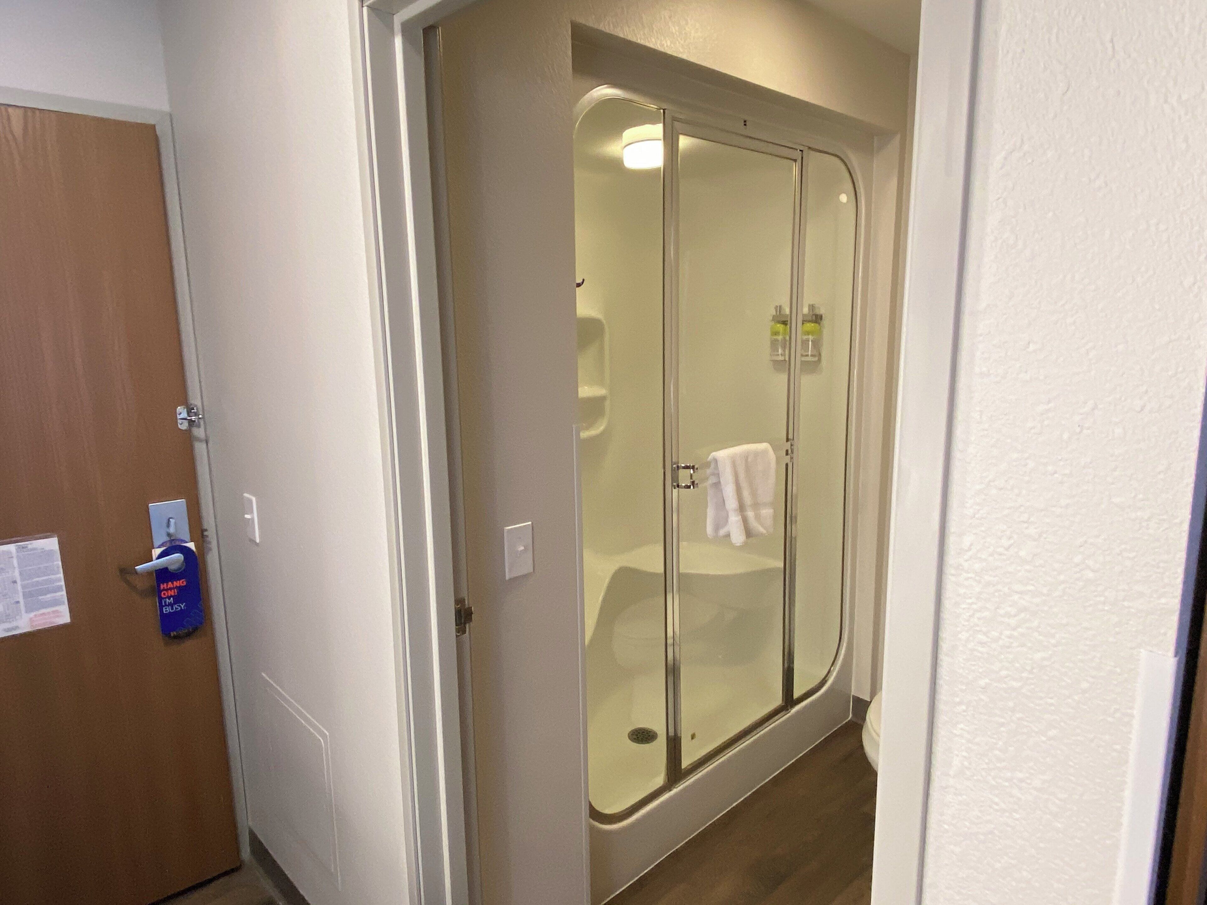 Un baño con ducha acristalada, una toalla colgada en la pared y una puerta con el letrero 'Hang On'.