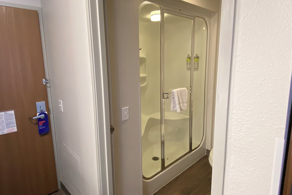Une salle de bain avec une douche en verre, une serviette accrochée au mur et une porte sur laquelle est affiché un panneau indiquant « Ne pas déranger ».