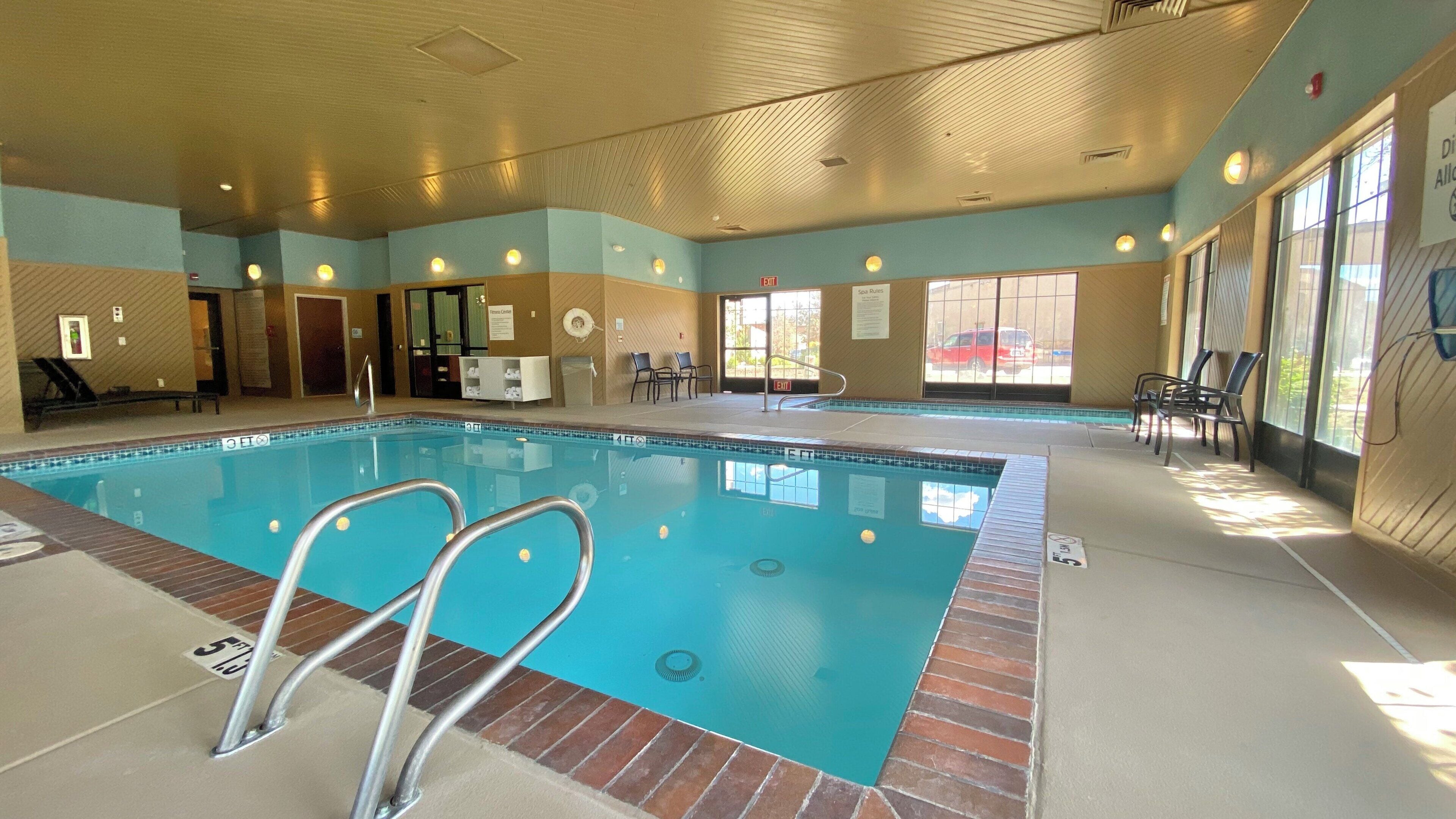 Une piscine intérieure à l’eau claire, entourée de murs percés de fenêtres et de portes, et dotée d’un plafond avec des luminaires encastrés.