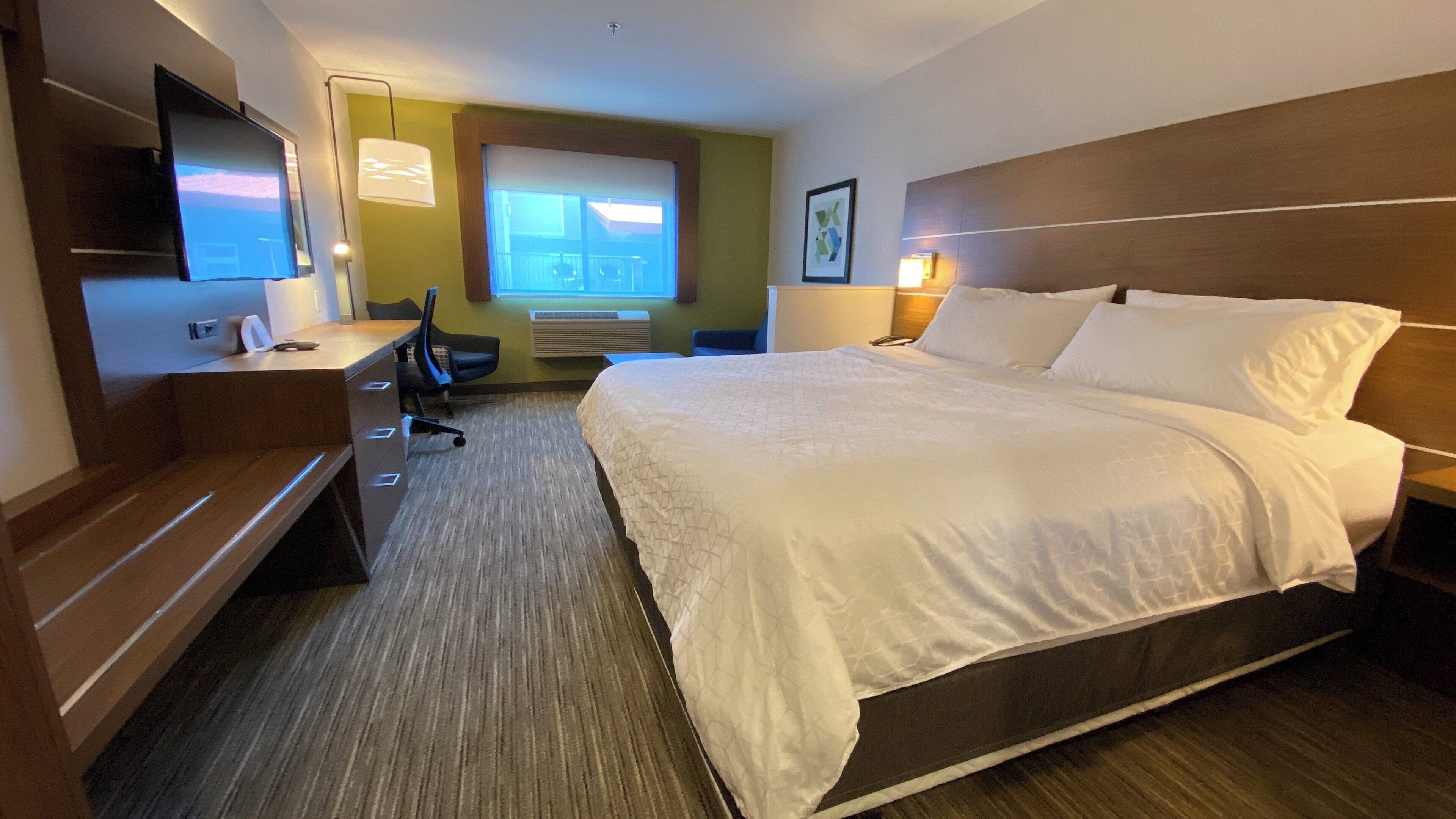 A hotel room with a large bed, a desk with a chair, a television, and a window with a view.
