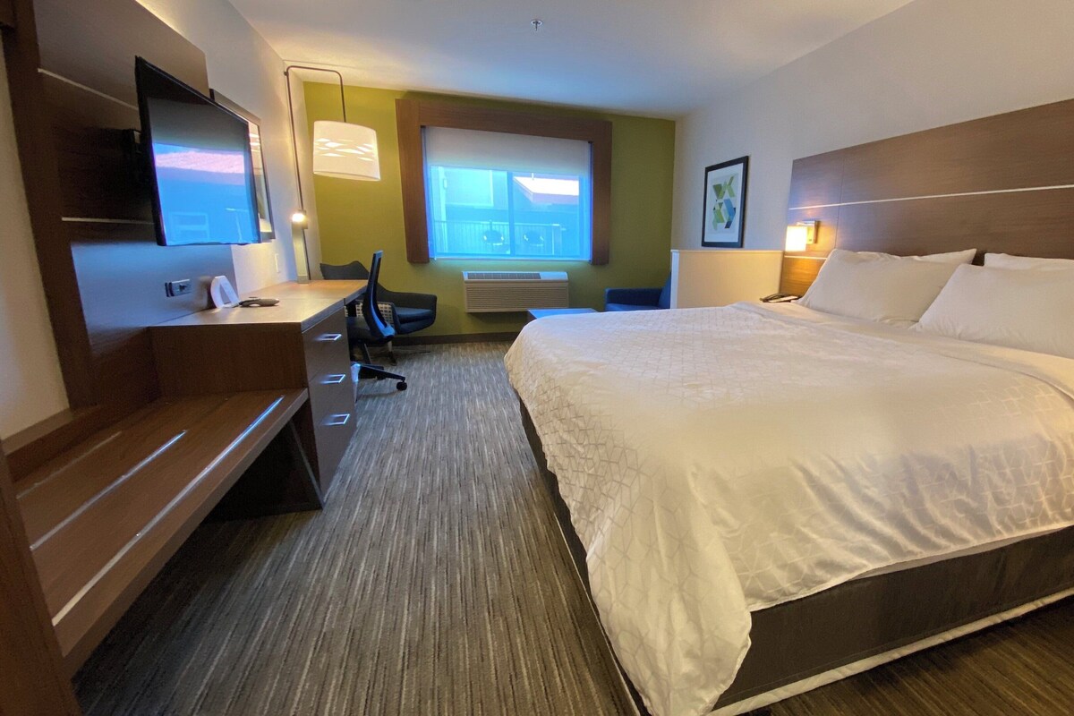 Une chambre d’hôtel avec un grand lit, un bureau avec une chaise, une télévision et une fenêtre donnant sur un beau paysage.