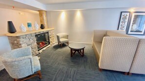 Un salon avec une cheminée en pierre, deux fauteuils, un canapé et une table basse.