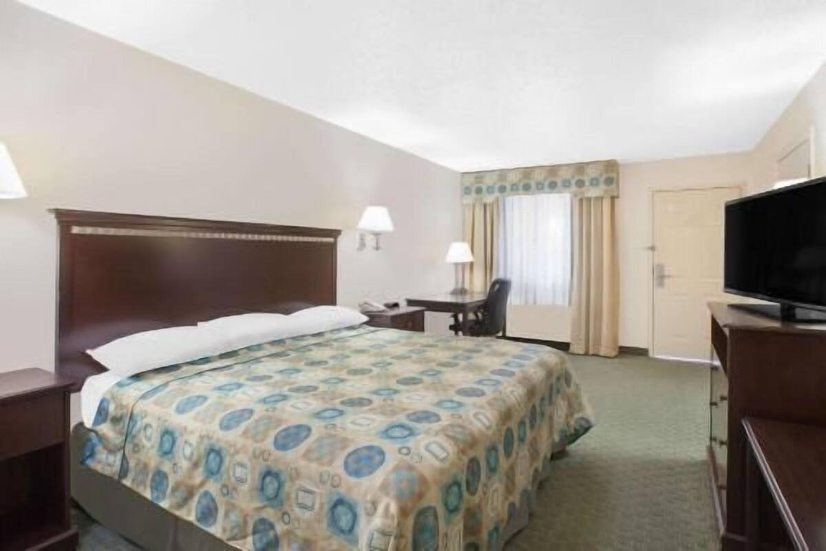 A hotel room with a bed, a desk, a chair, a television, and a door.
