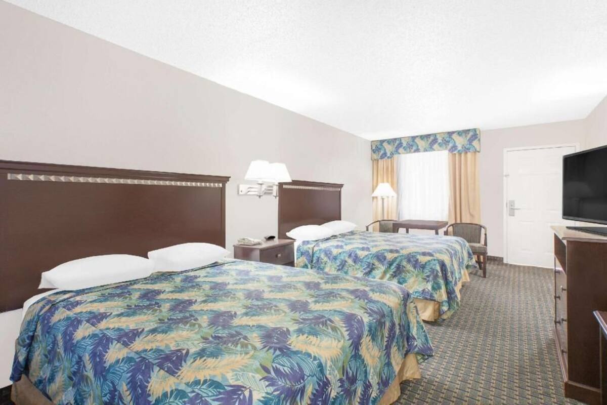 A hotel room with two beds, a desk, a chair, a television, and a window with curtains.