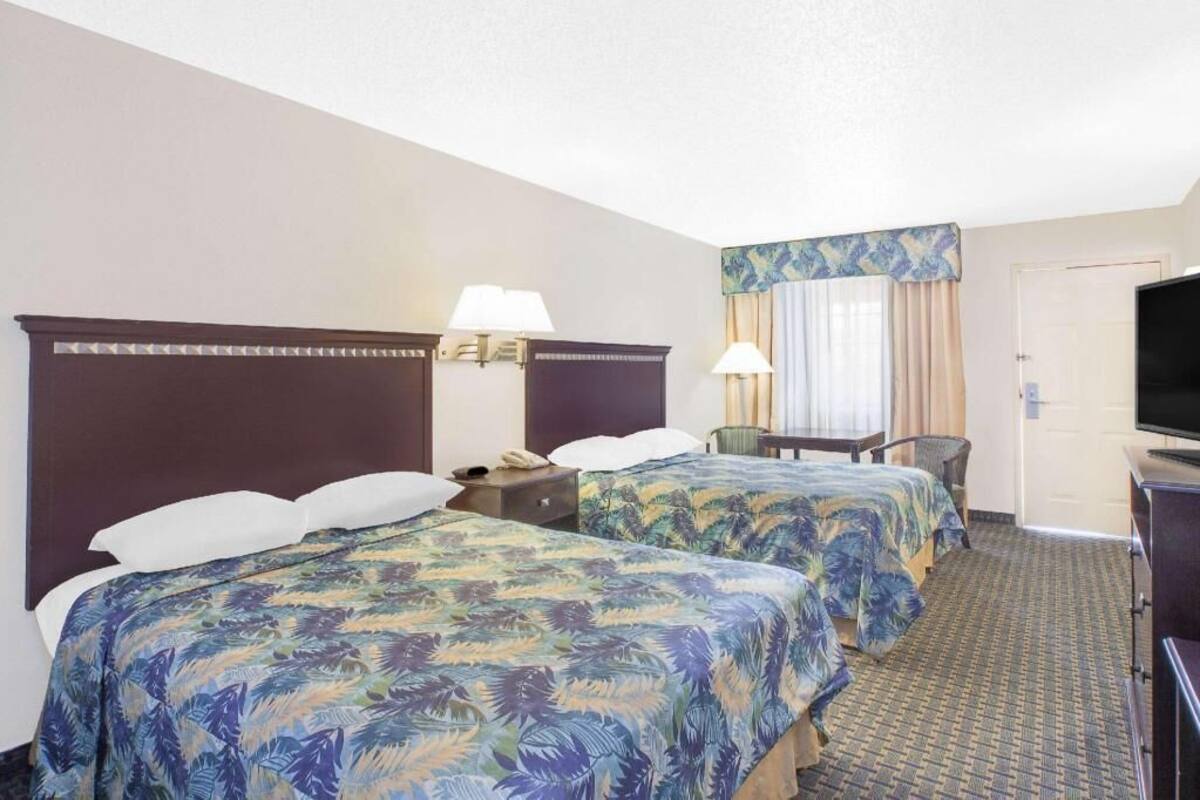 A hotel room with two beds, a desk, a chair, a television, and a door.