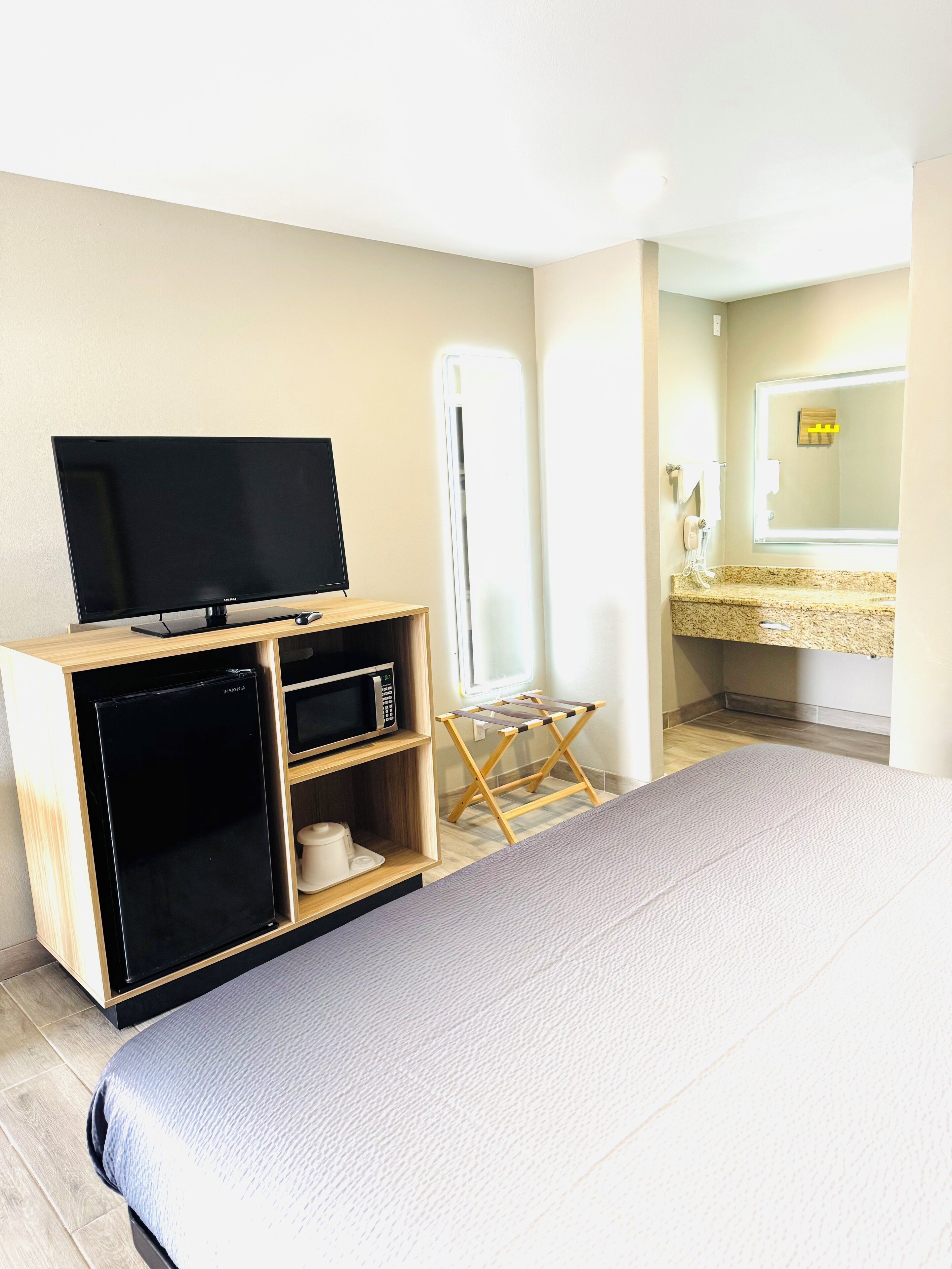 Una habitación de hotel con una cama, un televisor sobre un soporte de madera, un microondas y un refrigerador pequeño.