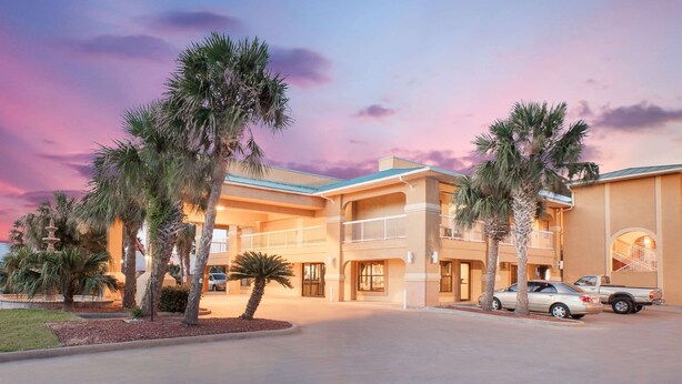 A hotel with a two-story structure, a covered parking area, and palm trees.