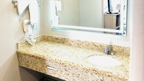 A bathroom with a granite countertop, a sink, a mirror, a hairdryer, and a towel rack.