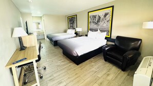 A hotel room with a bed, a desk with a chair, a black leather armchair, and two wall-mounted lamps.