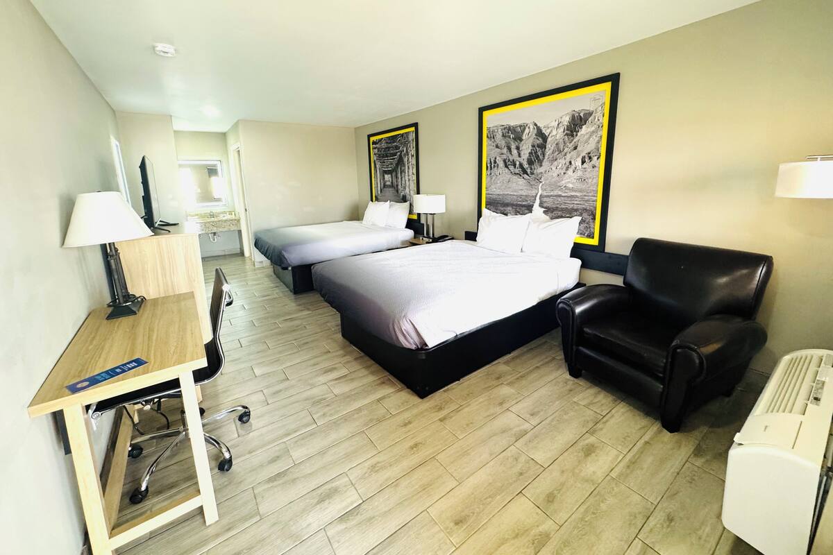 A hotel room with a bed, a desk with a chair, a black leather armchair, and two wall-mounted lamps.