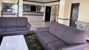 A lobby with two patterned sofas, a reception desk, a clock, and a door.