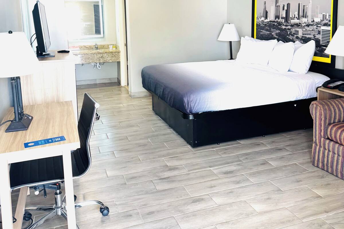 A hotel room with a bed, desk, chair, and a cityscape painting on the wall.