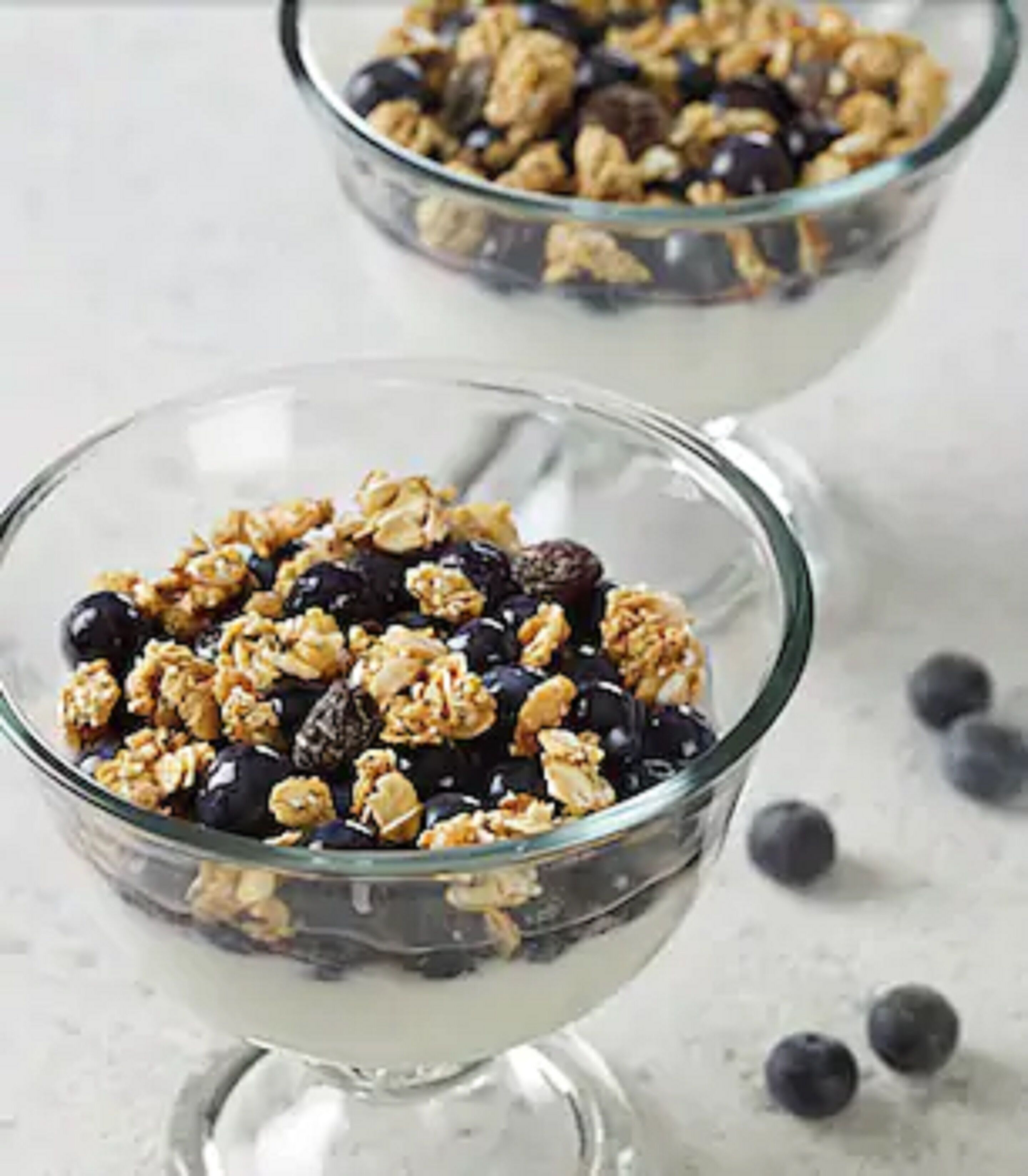 Two clear glass bowls filled with granola and blueberries.