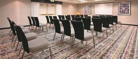 A conference room with rows of chairs, a projector screen, and an exit sign.
