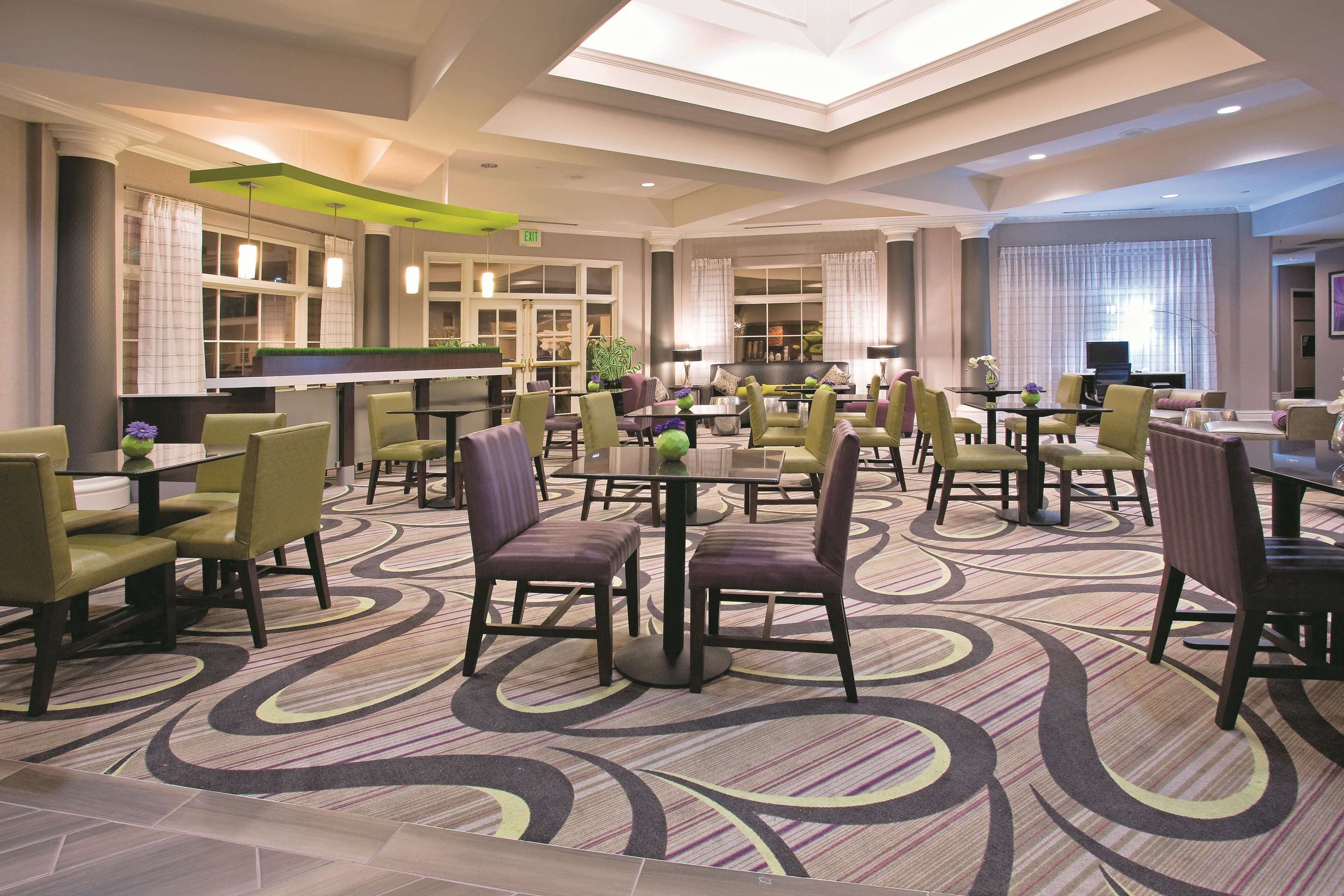 A hotel lobby with multiple seating areas, a reception desk, and a large window with curtains.
