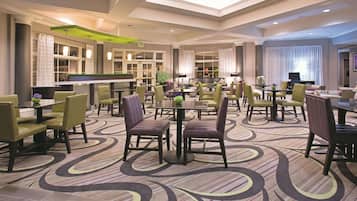 A hotel lobby with multiple seating areas, a reception desk, and a large window with curtains.