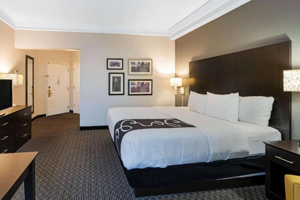 Une chambre d’hôtel avec un grand lit, un bureau, une chaise, une télévision et des tableaux encadrés au mur.