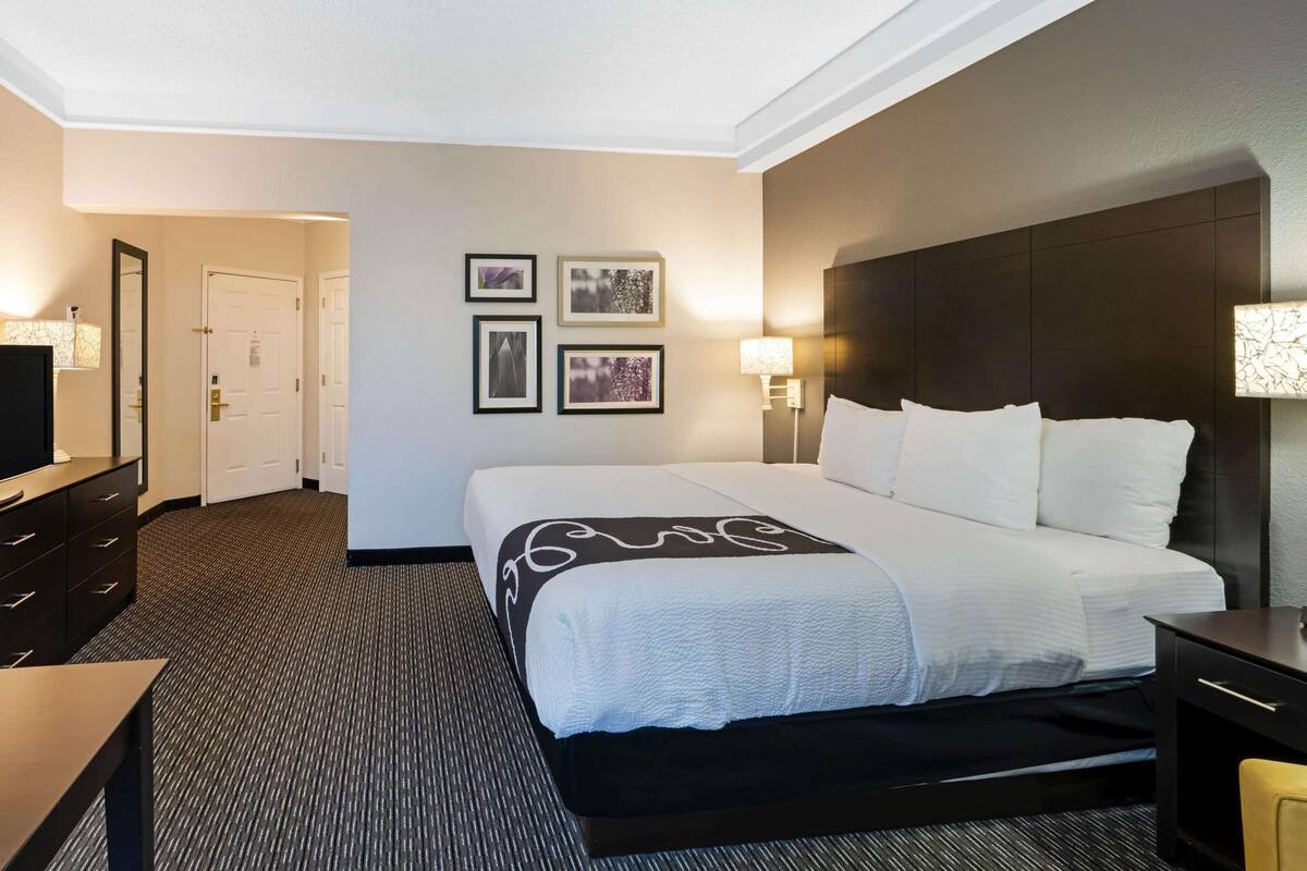 Une chambre d’hôtel avec un grand lit, un bureau, une chaise, une télévision et un mur orné de tableaux.