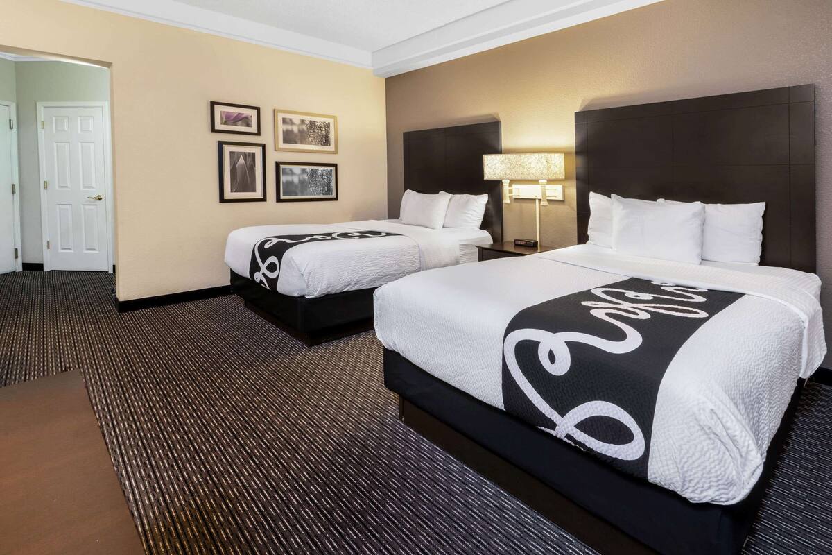 Une chambre d’hôtel avec deux lits, une porte et des tableaux encadrés au mur.