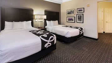 Quarto de hotel com duas camas, cabeceira escura, piso coberto de carpete e quadros nas paredes.