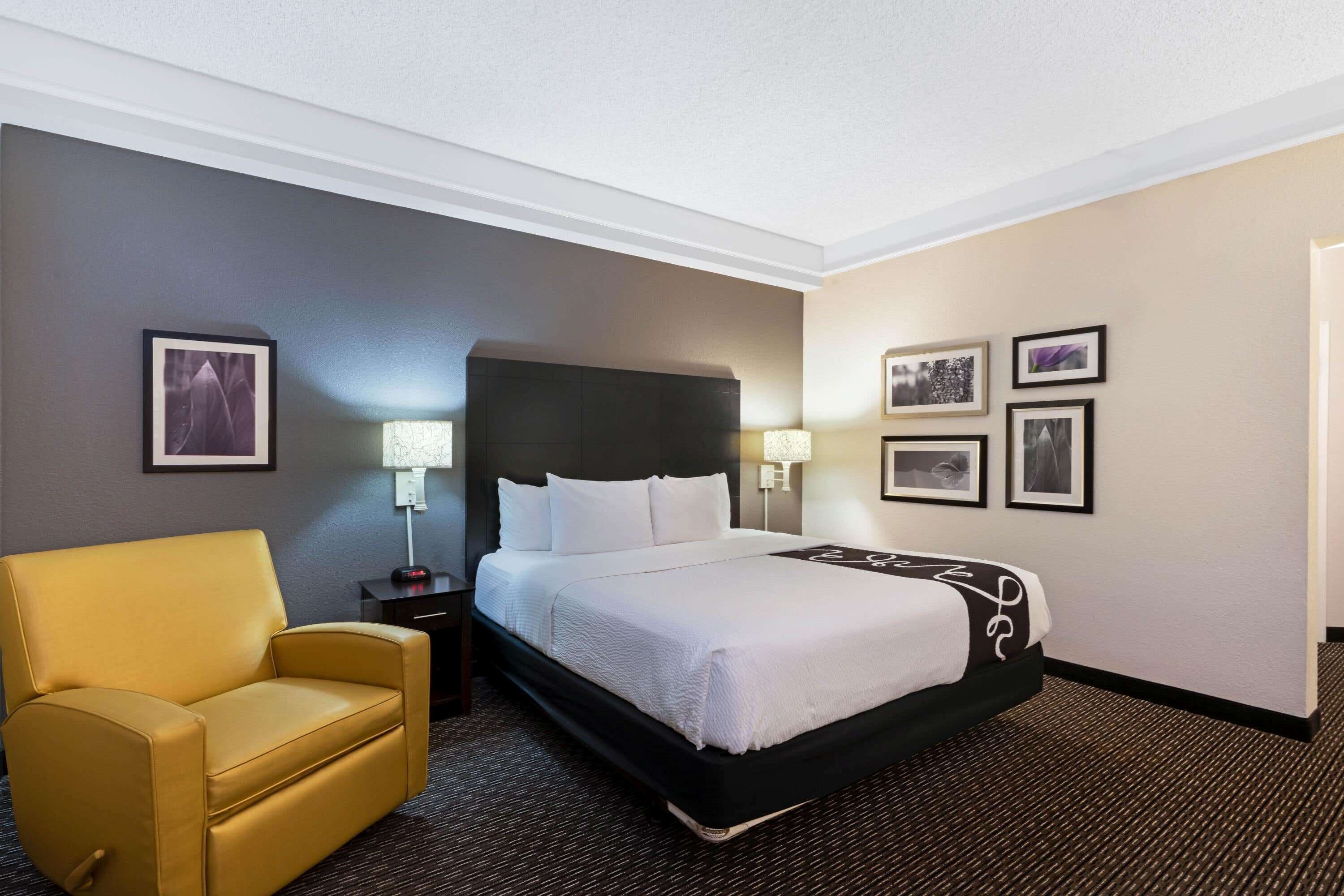 Quarto de hotel com uma cama, uma cadeira e uma mesa de cabeceira com abajur.