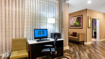 A hotel room with a desk, computer, and a sofa.